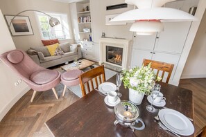 Ein gemütliches Wohnzimmer mit Kamin, einem Essbereich mit Tisch für zwei Personen und einem rosa Sessel.
