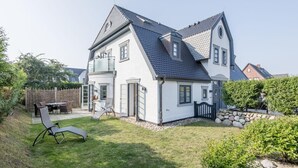 Kaksikerroksinen talo, jossa on parveke, ulkokalusteilla varustettu patio ja kivimuuri.