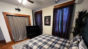 Ein Schlafzimmer mit einem Bett, einem Fernseher, einer Pflanze und einem gerahmten Bild an der Wand.