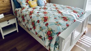 A bedroom with a wooden headboard, a white bed frame, and a floral bedspread. - Newly Renovated Ranch House with  Open Concept (Fredericksburg)