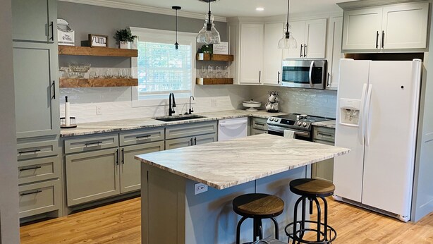 A modern kitchen with grey cabinets, a marble island, bar stools, pendant lights, and a view of the city through the window. - Newly Renovated Ranch House with  Open Concept (Fredericksburg)