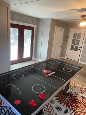 Uma mesa de bilhar em um quarto com uma porta, um extintor e um ventilador de teto.