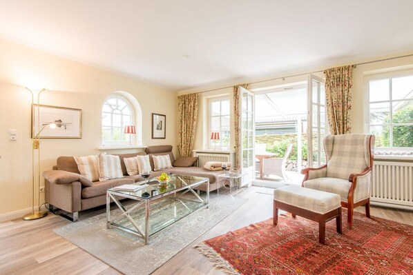 A living room with a sofa, armchair, coffee table, and a view of the outdoors through large windows. - House at Wenningstedter Weg 12, Half B (Sylt)