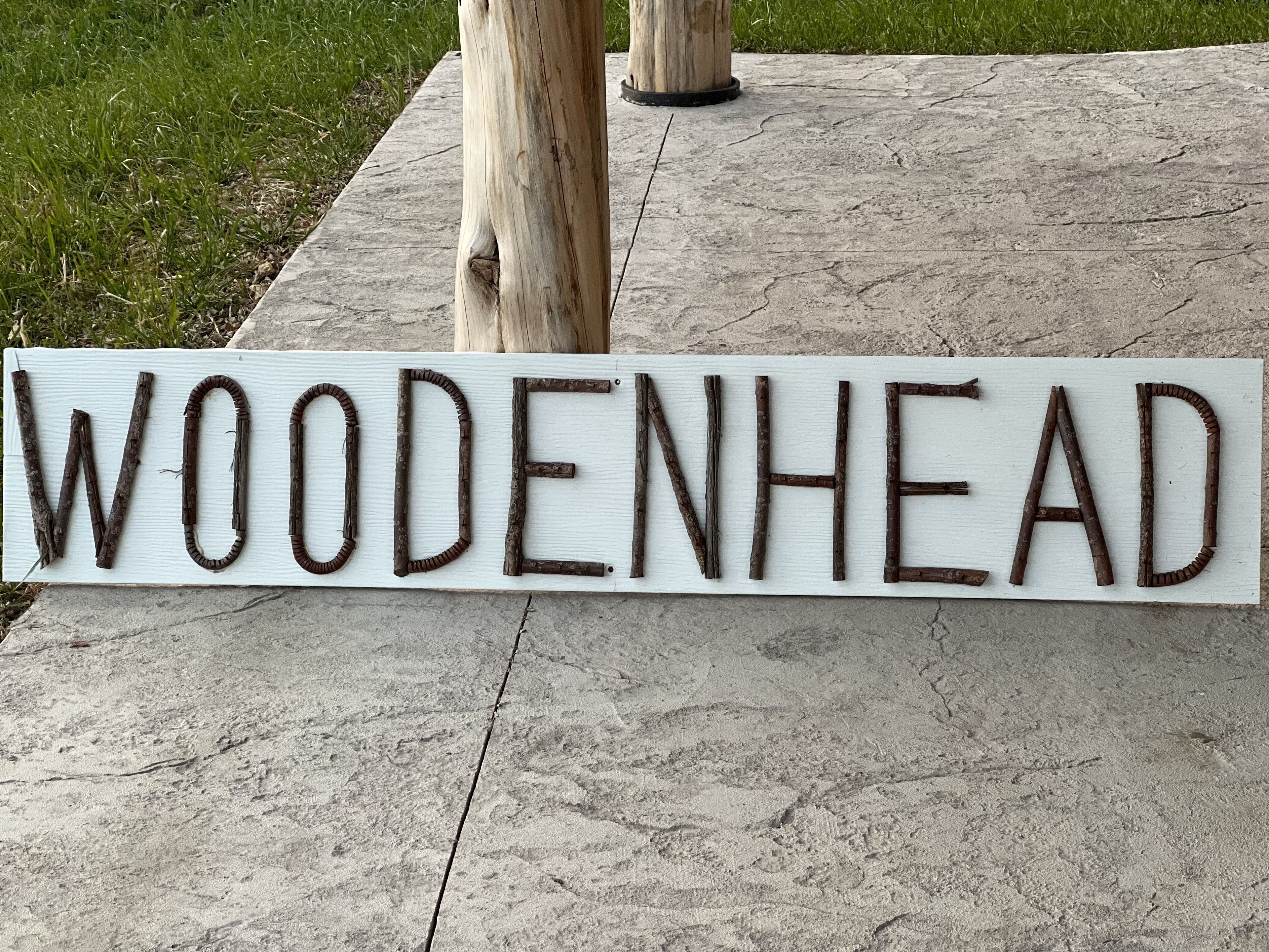Un letrero de madera con la palabra 'WOODENHEAD' sobre una superficie de concreto.
