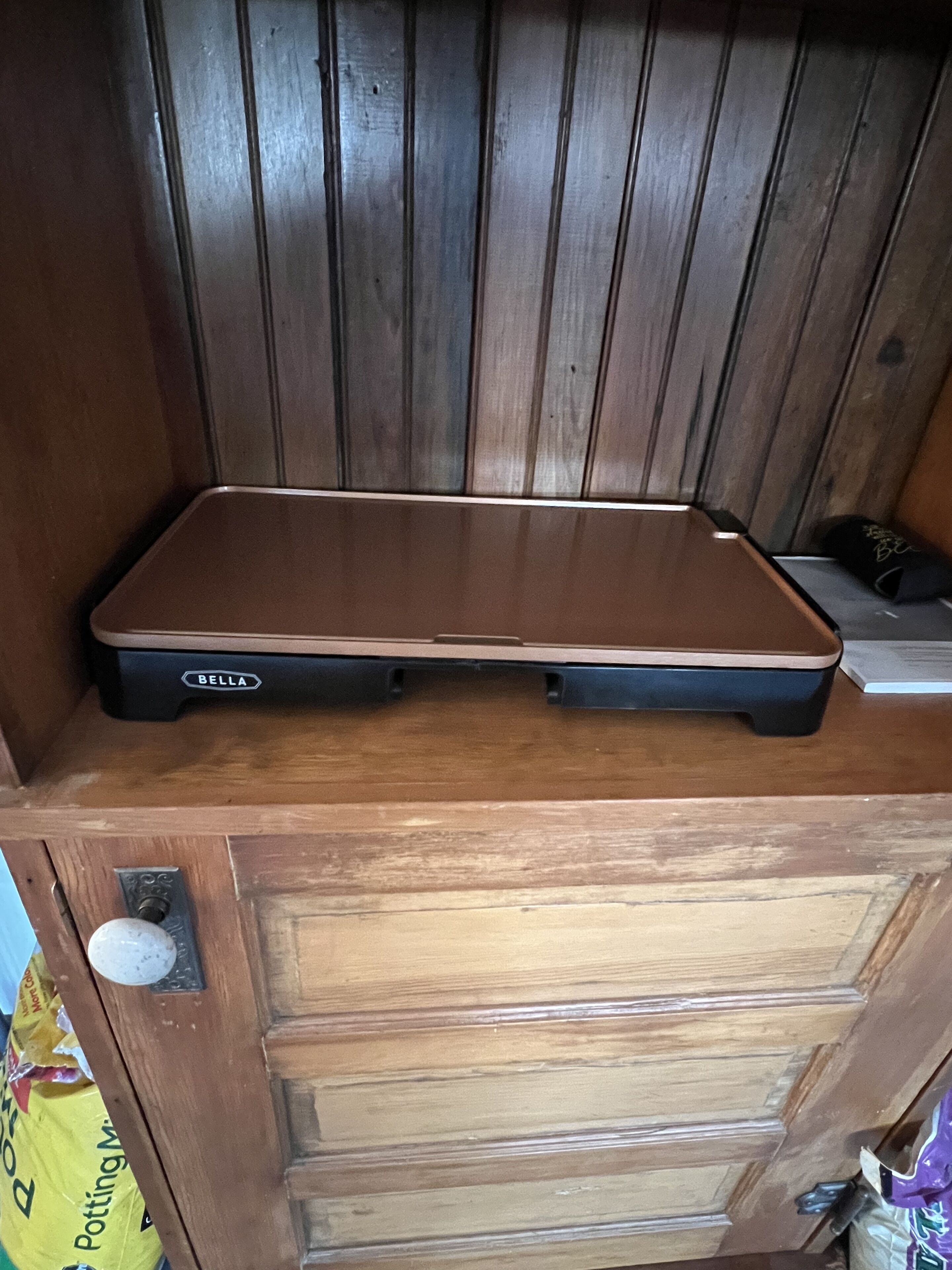 A wooden cabinet with a flat surface on top, a drawer below, and a bag of Potting Mix to the left.