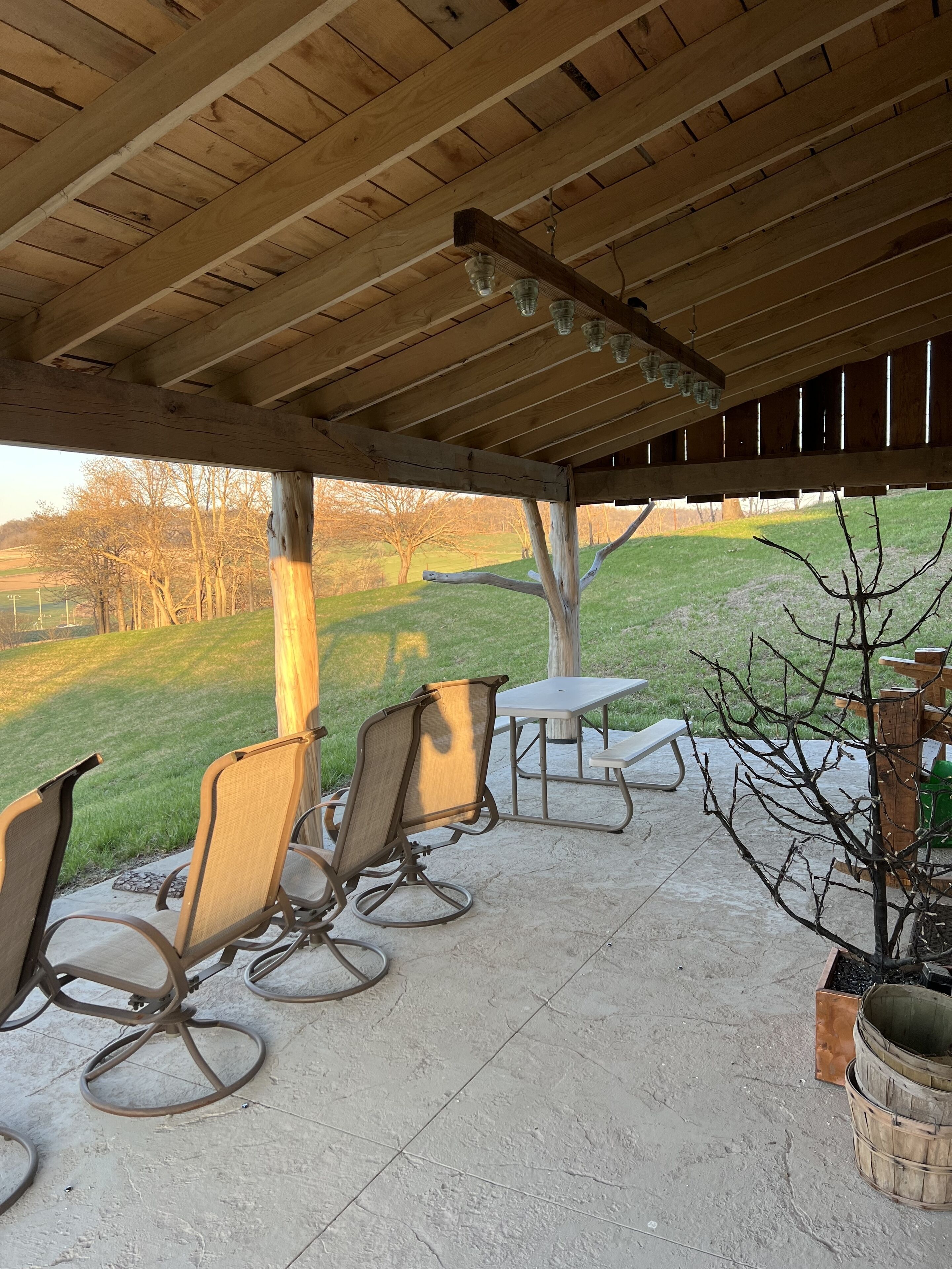 A covered patio with outdoor furniture, a table, and a view of a grassy landscape.