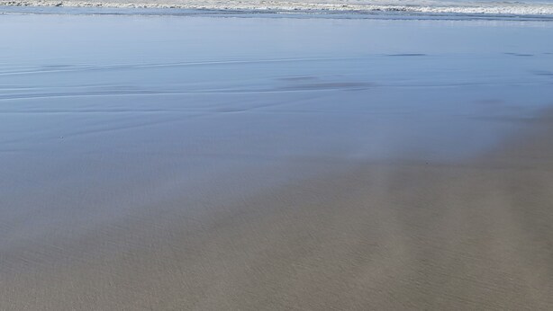 Ein Strand mit feuchtem Sand und Wellen im Hintergrund.