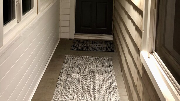 A narrow hallway with wooden ceiling and walls, a dark door, and a welcome mat. - Cozy SK Cottage 💜 (South Kingstown)