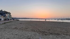 A beach with a row of buildings on the left, a sandy shore, and boats in the water.