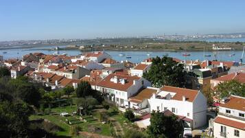 Une ville côtière aux bâtiments blancs et aux toits rouges, un port de plaisance avec des bateaux, et une vue dégagée sur la mer et le lointain horizon urbain.