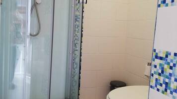 A bathroom with a glass-enclosed shower, a toilet, and tiled walls.