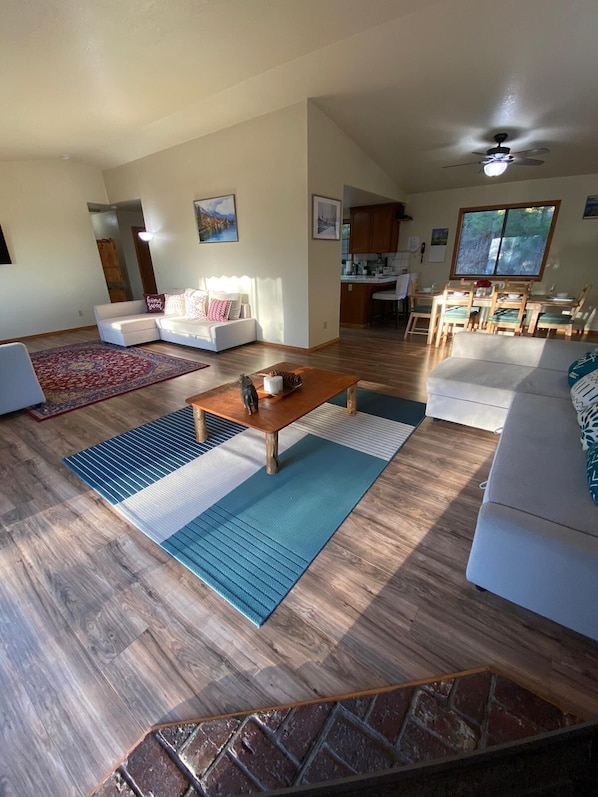 A spacious living room with a wooden floor, a coffee table, a sofa, and a dining area with a table and chairs.