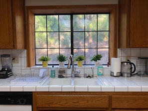 A kitchen with a large window, wooden cabinets, a sink, a dishwasher, and various kitchen appliances.