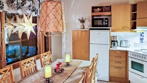A kitchen with wooden cabinets, a refrigerator, a stove, and a dining table with chairs. - Alppitalo sinitähti 9 as 3 by Interhome (Nilsiä)