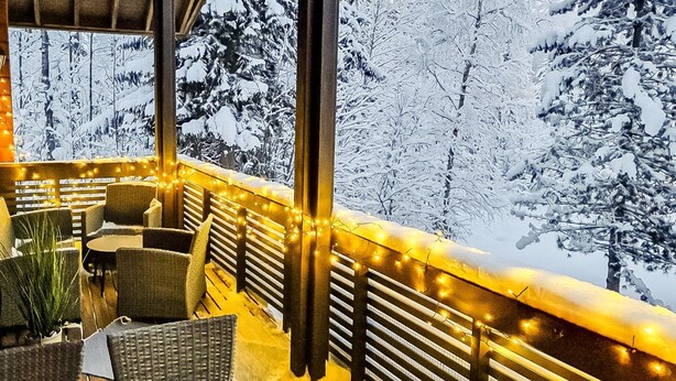 A covered outdoor seating area with wicker furniture and string lights, overlooking a snowy forest. - Alppitalo sinitähti 9 as 3 by Interhome (Nilsiä)