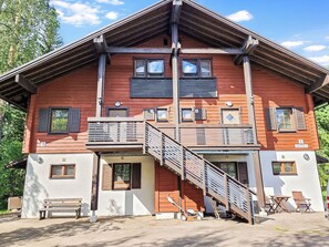 Un immeuble en bois à plusieurs étages, doté de balcons, d’un escalier et d’un espace extérieur aménagé pour s’asseoir.
