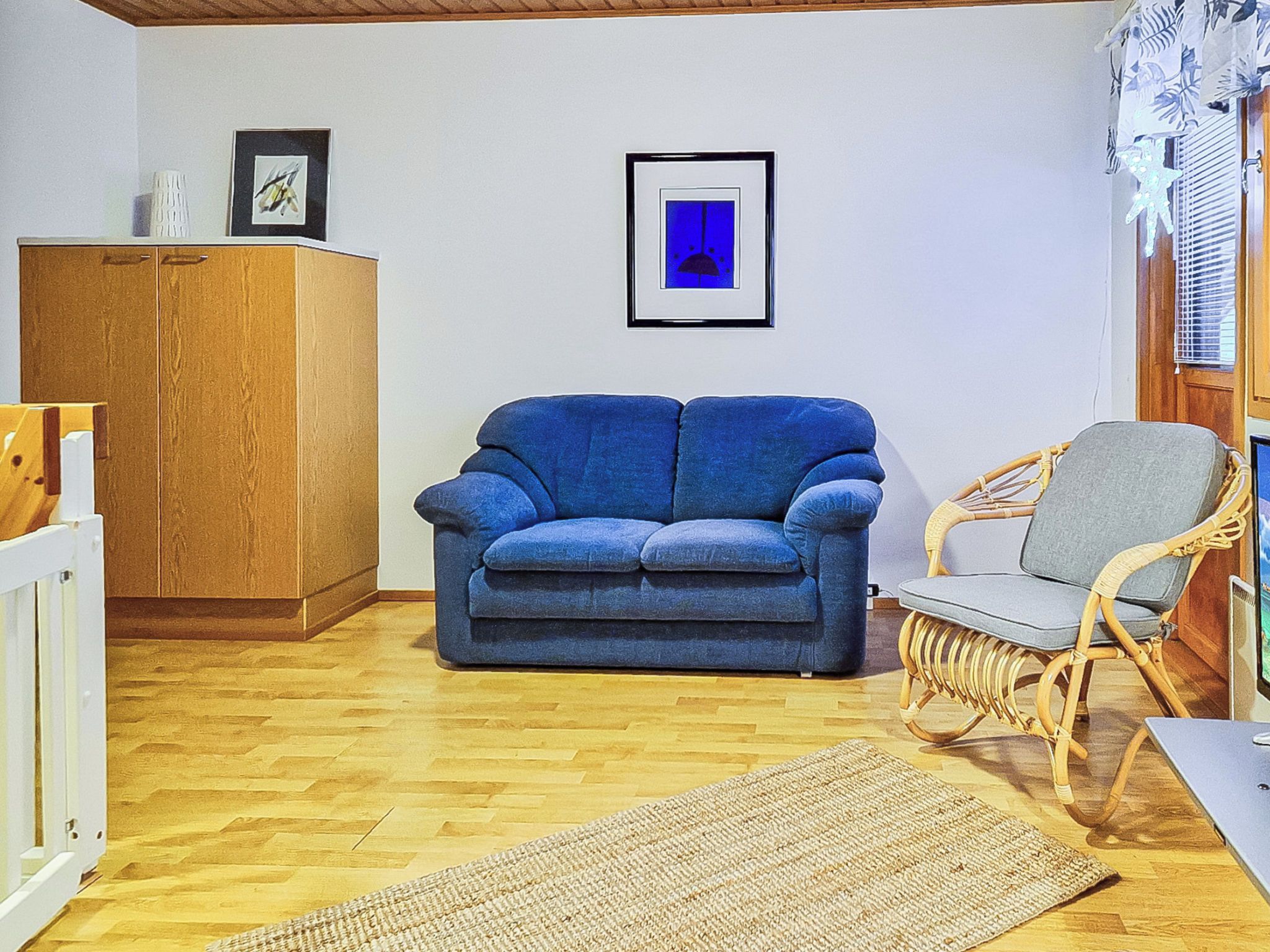 A living room with a blue sofa, a wicker chair, a wooden cabinet, and a framed picture on the wall.