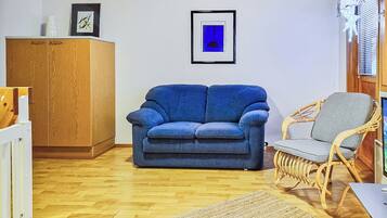 A living room with a blue sofa, a wicker chair, a wooden cabinet, and a framed picture on the wall.
