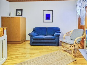 A living room with a blue sofa, a wicker chair, a wooden cabinet, and a framed picture on the wall. - Alppitalo sinitähti 9 as 3 by Interhome (Nilsiä)