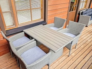 Une terrasse en bois avec une table et six chaises en osier dotées de coussins.