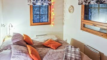 A bedroom with a bed, pillows, a window with blinds, a wall clock, and a radiator.