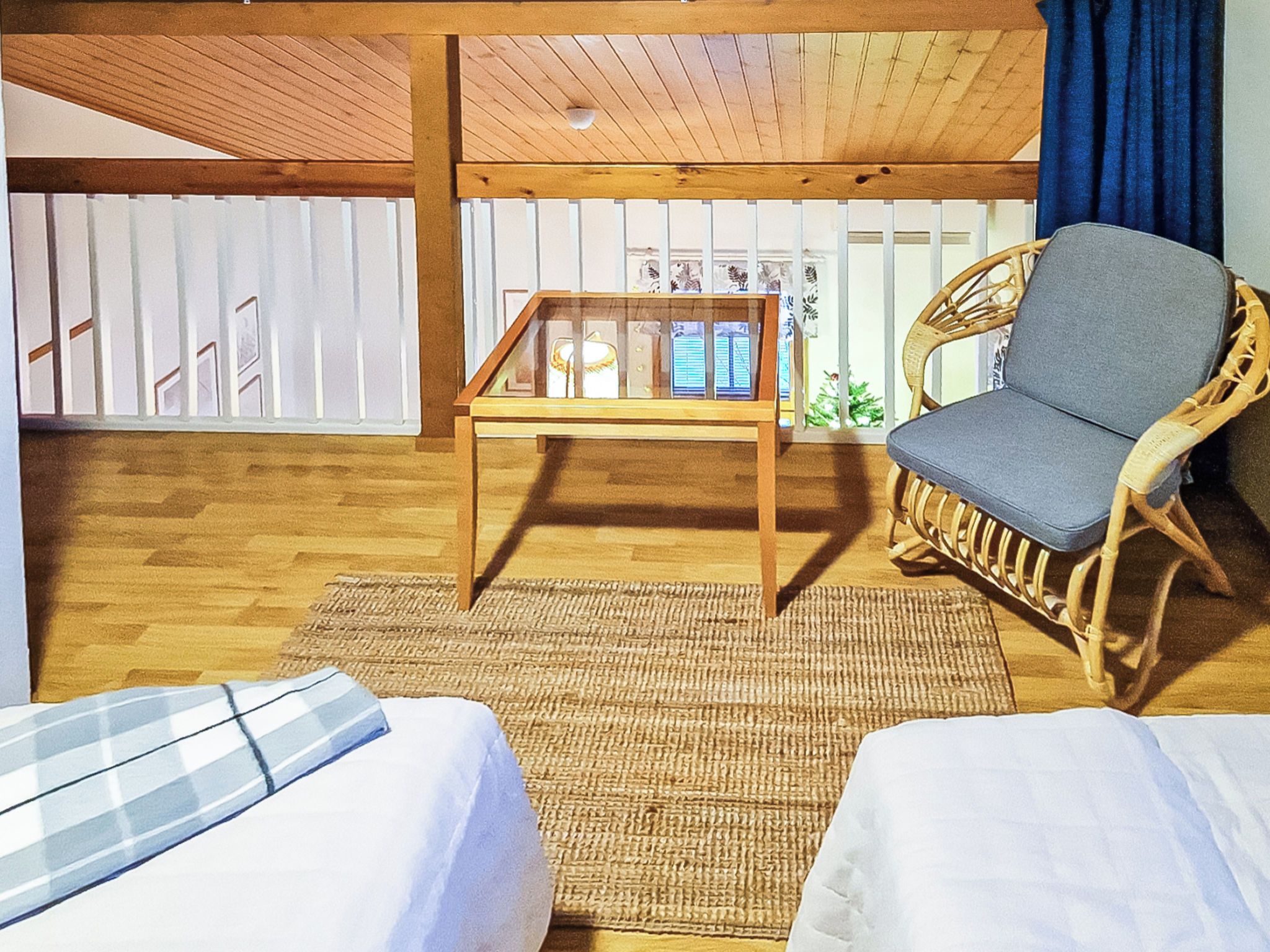 Una habitación con dos camas, una mesa con pantalla, una silla de mimbre y vistas a una valla blanca.
