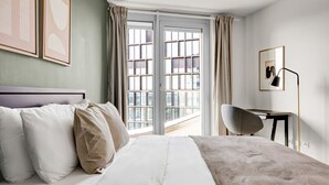 Een hotelkamer met een bed, een bureau en uitzicht op de stad door grote ramen.