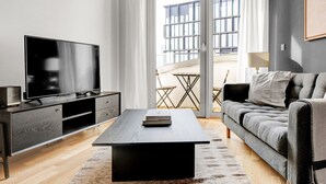 Een moderne woonkamer met een flatscreen televisie, een donker houten salontafel, een grijze bank en een balkon met een tafel en stoelen.