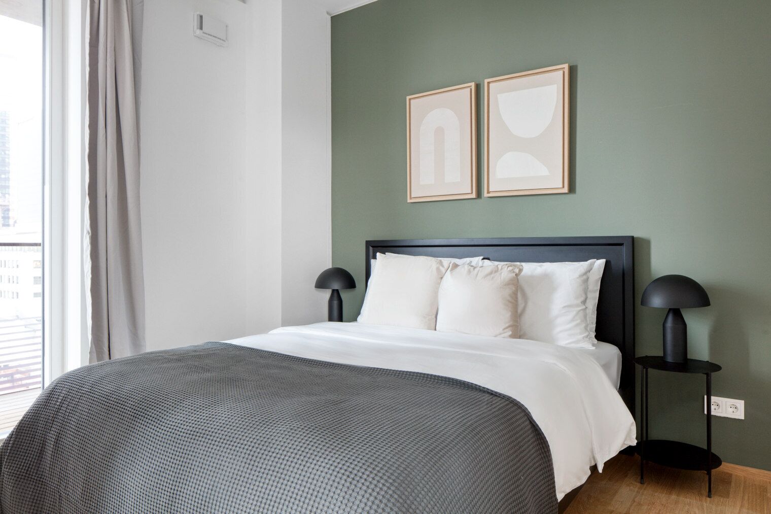 Una cama bien hecha con un edredón gris, dos lámparas de noche y dos cuadros en la pared.