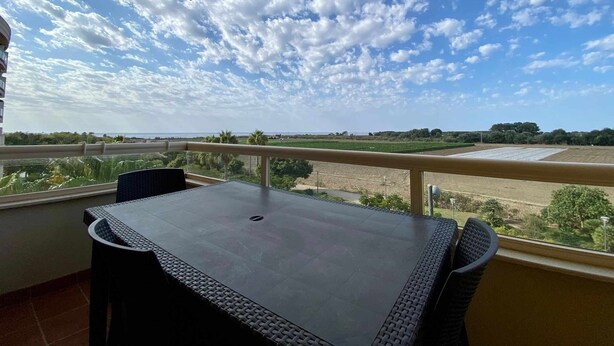 Ein Balkon mit Tisch und Stühlen, der auf eine Landschaft mit Feldern und einer entfernten Küste blickt.