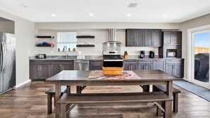 A modern kitchen with dark cabinets, a stainless steel refrigerator, a built-in oven, and a large dining table with benches. - Beachfront | Pet Friendly | Heated Pool (Gulf Shores)