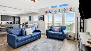 A spacious living room with a blue leather sofa, a patterned rug, and a ceiling skateboard. - Beachfront | Pet Friendly | Heated Pool (Gulf Shores)