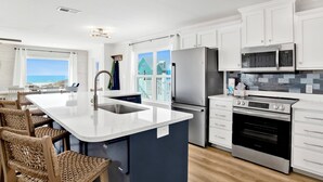 A modern kitchen with white cabinets, stainless steel appliances, and a large island with seating. - Gulf Views | Private Heated Pool | Pet Friendly (Gulf Shores)