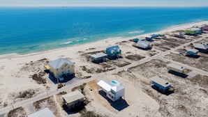 An aerial view of a coastal area with multiple buildings, some elevated on stilts, near a beach with clear blue waters. - Gulf Views | Private Heated Pool | Pet Friendly (Gulf Shores)