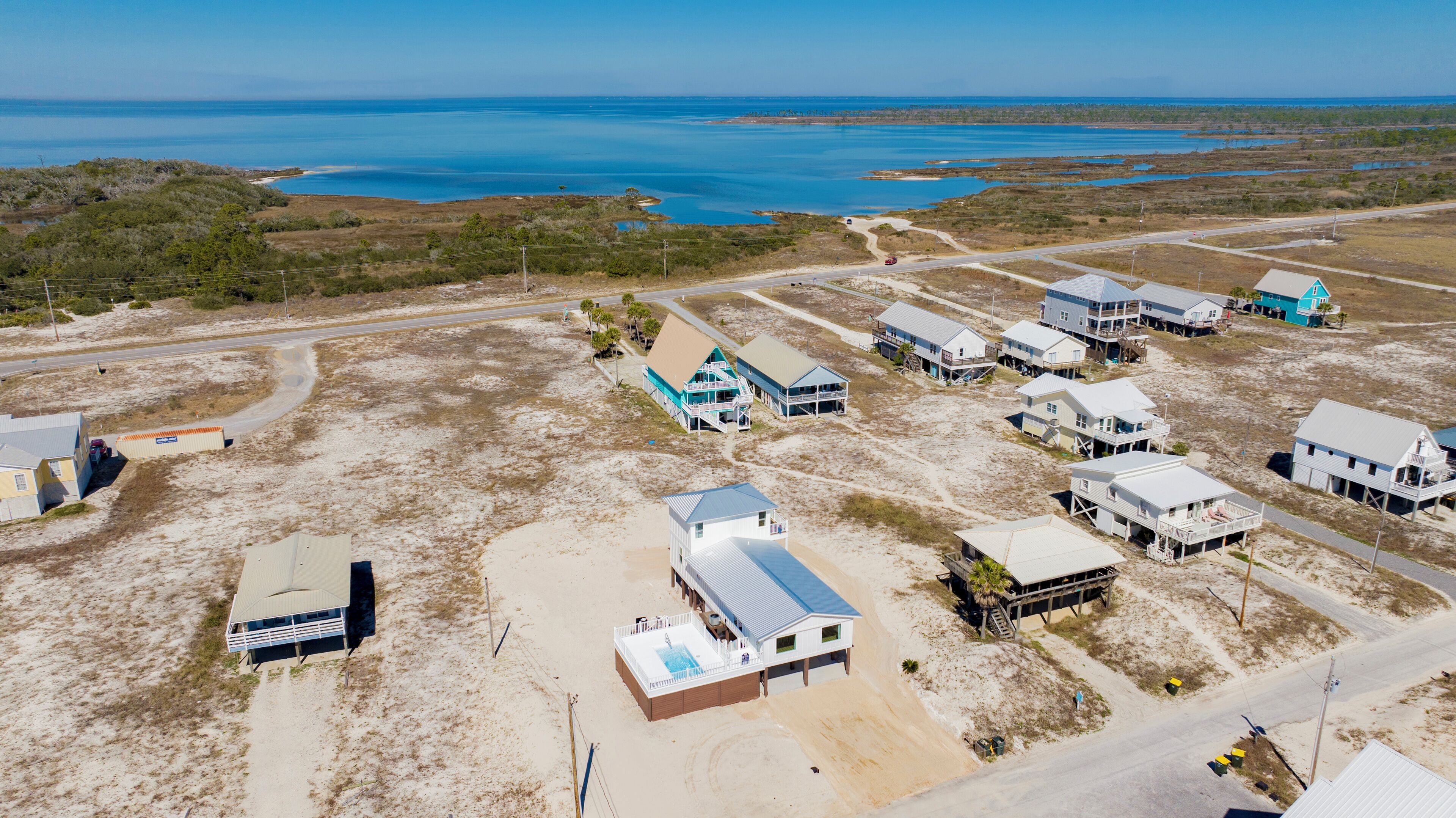 An aerial view of a coastal area with several beachfront properties, including houses with balconies and a large building with a swimming pool.