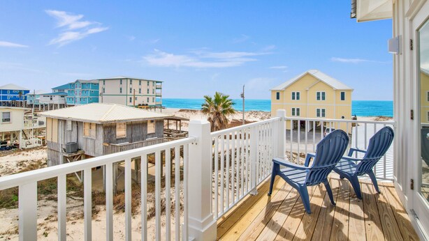 A wooden deck with two chairs overlooking a beach with buildings in the background. - Gulf Views | Private Heated Pool | Pet Friendly (Gulf Shores)