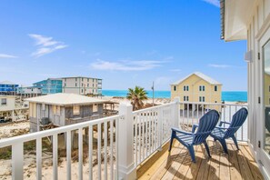 A wooden deck with two chairs overlooking a beach with buildings in the background. - Gulf Views | Private Heated Pool | Pet Friendly (Gulf Shores)