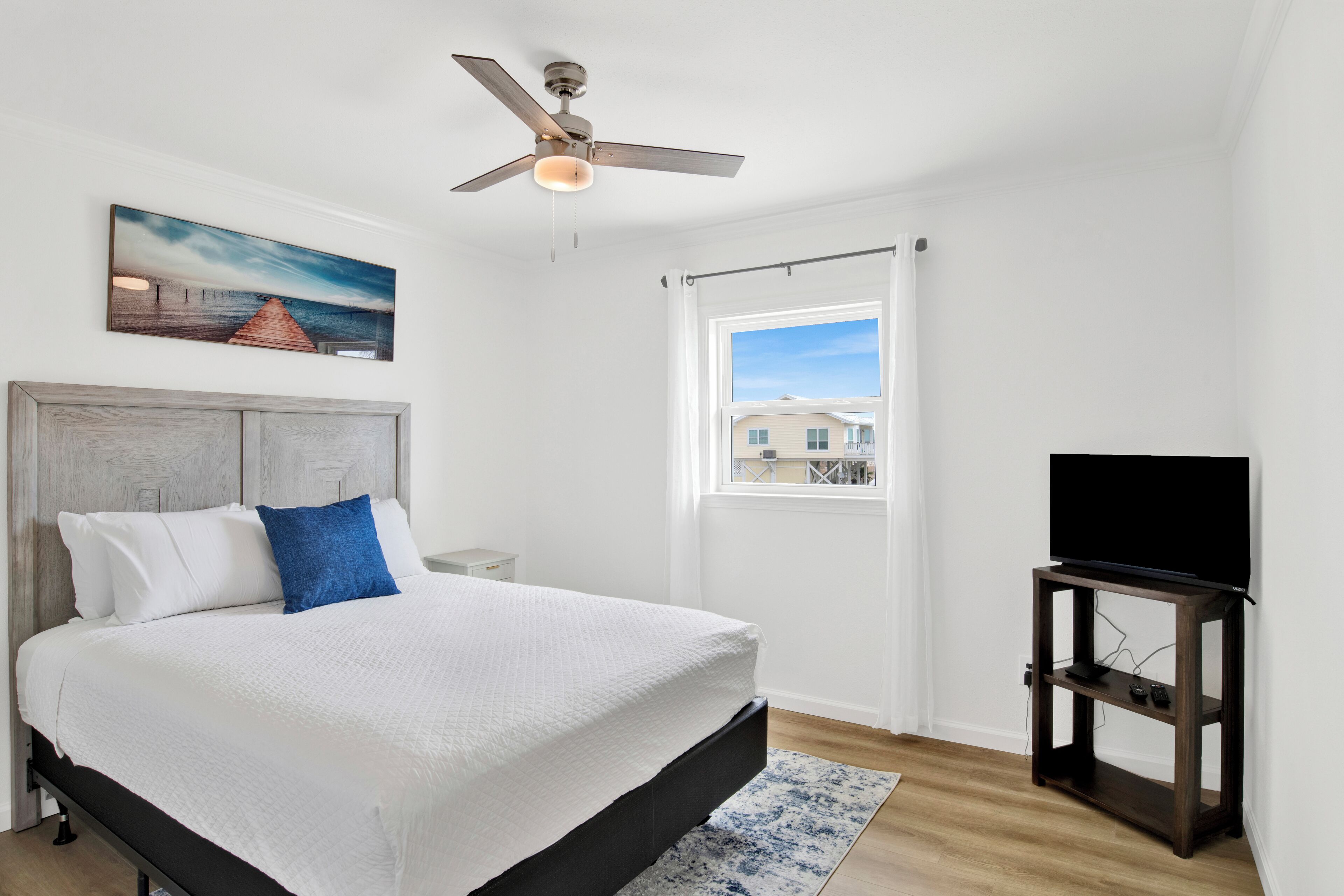 A bedroom with a bed, a ceiling fan, a window with curtains, and a TV on a stand.