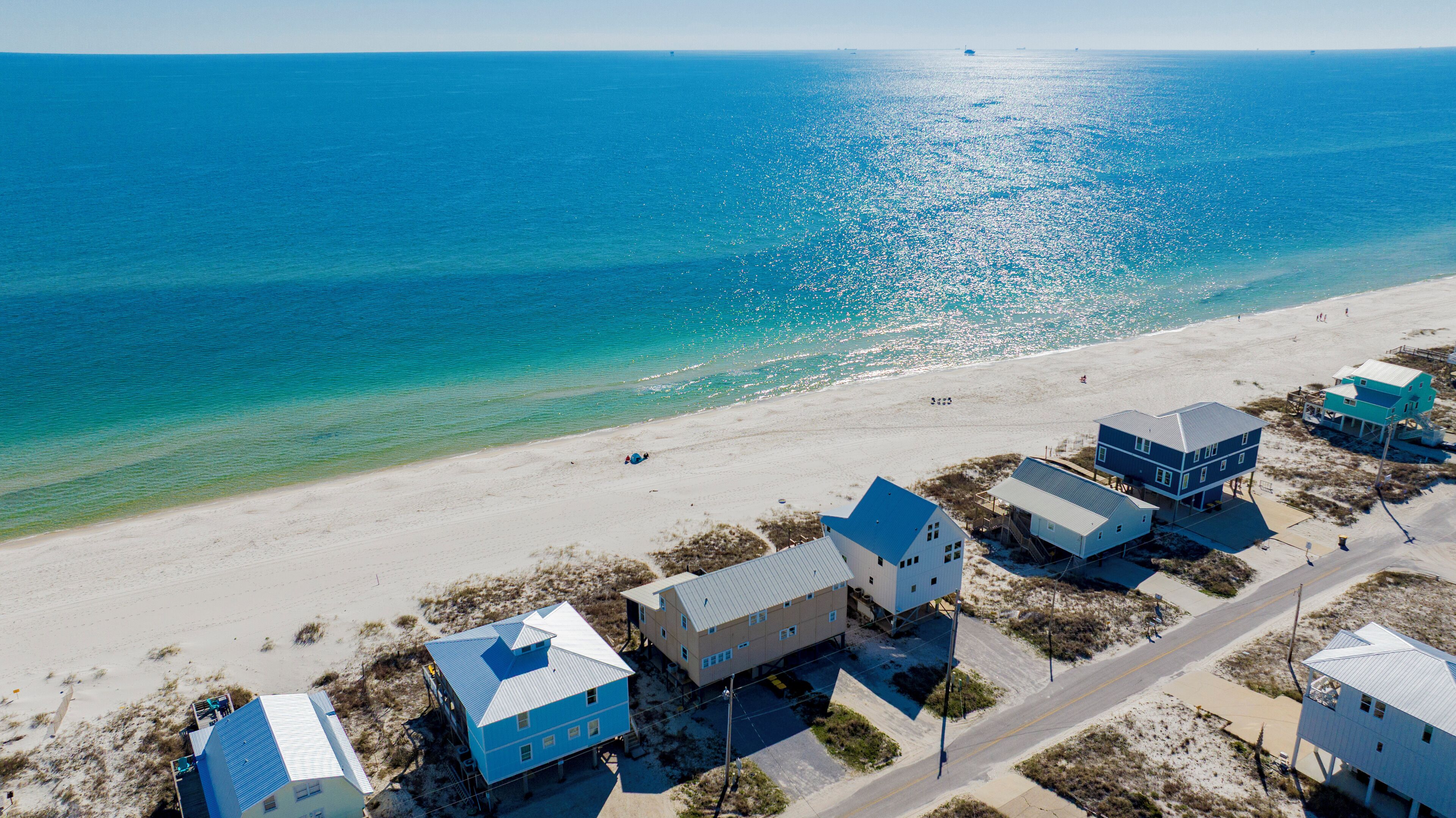An aerial view of a beachside property with multiple houses, a clear view of the ocean, and a sandy beach.