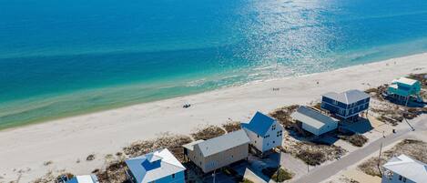 An aerial view of a beachside property with multiple houses, a clear view of the ocean, and a sandy beach.
