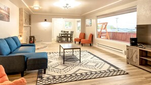 Un salon avec un canapé bleu, des fauteuils orange, une table basse et un téléviseur posé sur un meuble en bois.