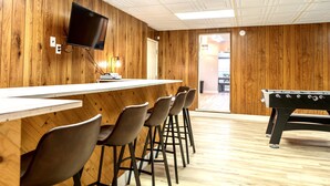 Un espace bar avec des murs en bois, un téléviseur à écran plat fixé au-dessus du bar et une table de baby-foot.