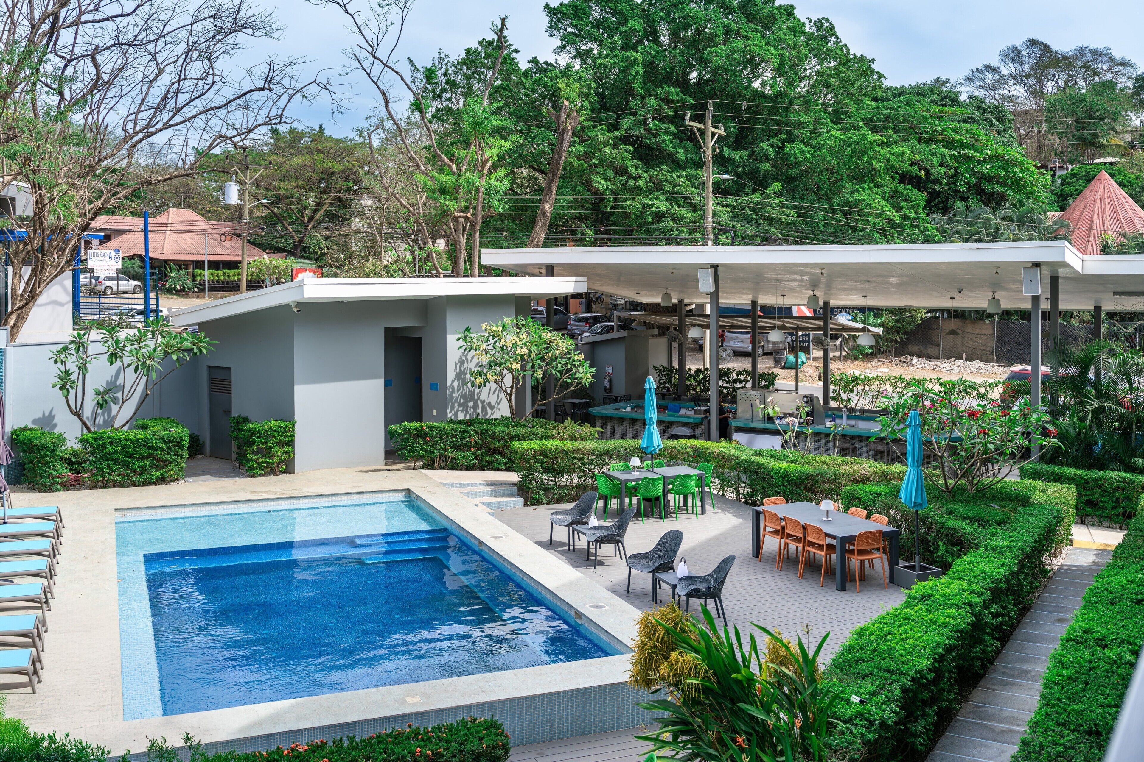 A swimming pool with lounge chairs, a covered outdoor seating area, and lush greenery.