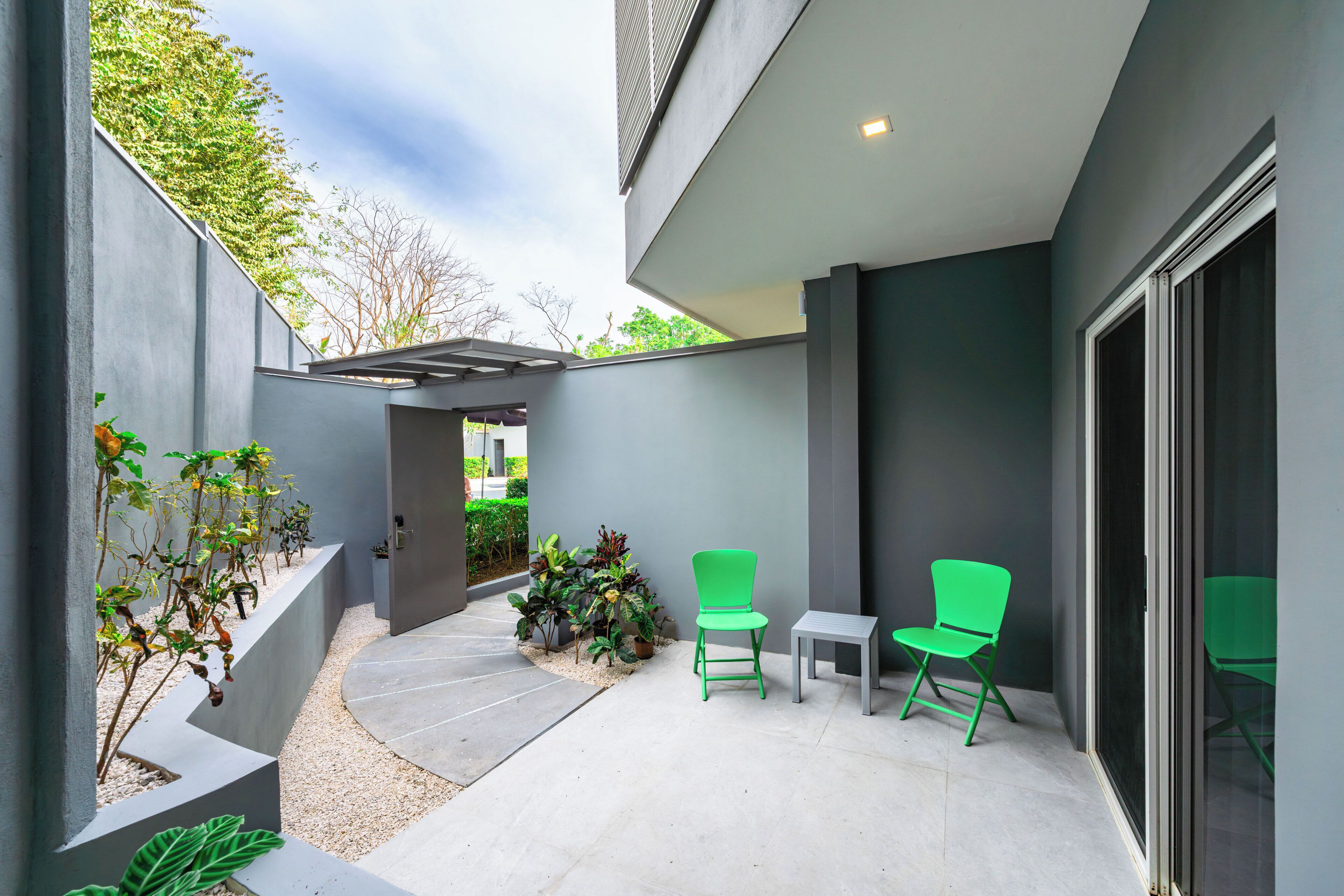 Une terrasse extérieure moderne avec un sol en béton, des chaises vertes et des plantes en pot.