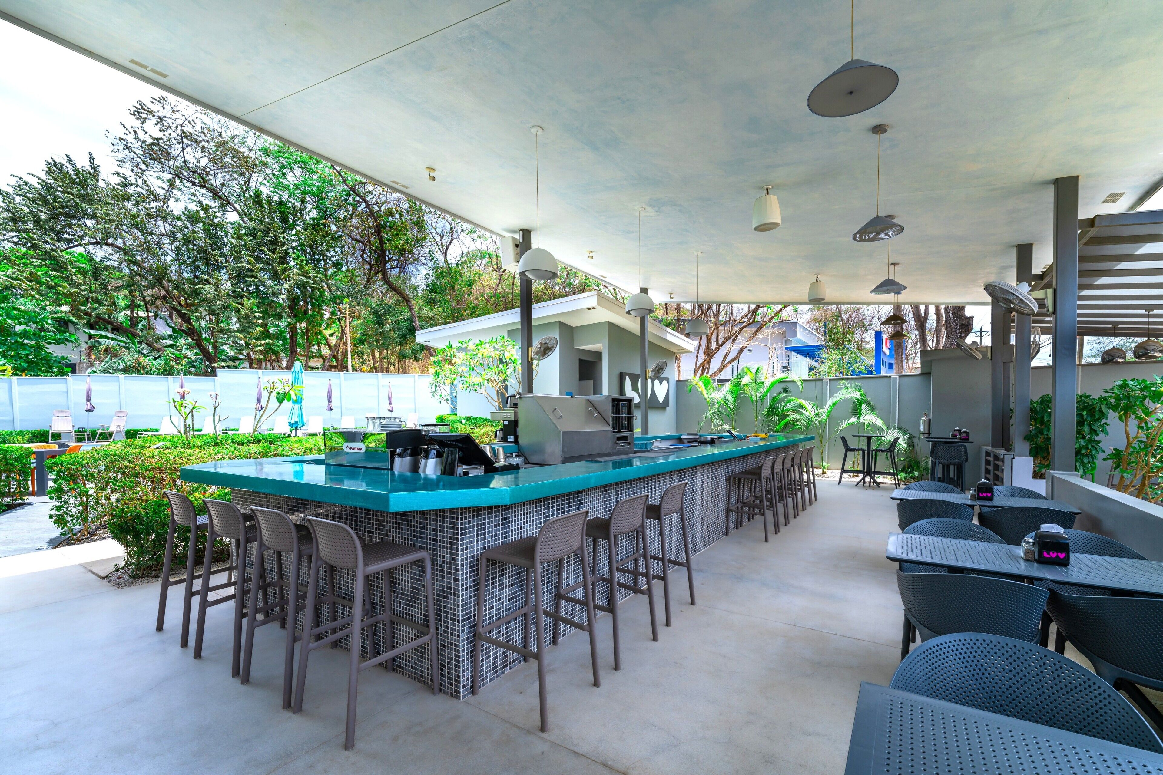 An outdoor bar area with a long counter, multiple bar stools, and tables.