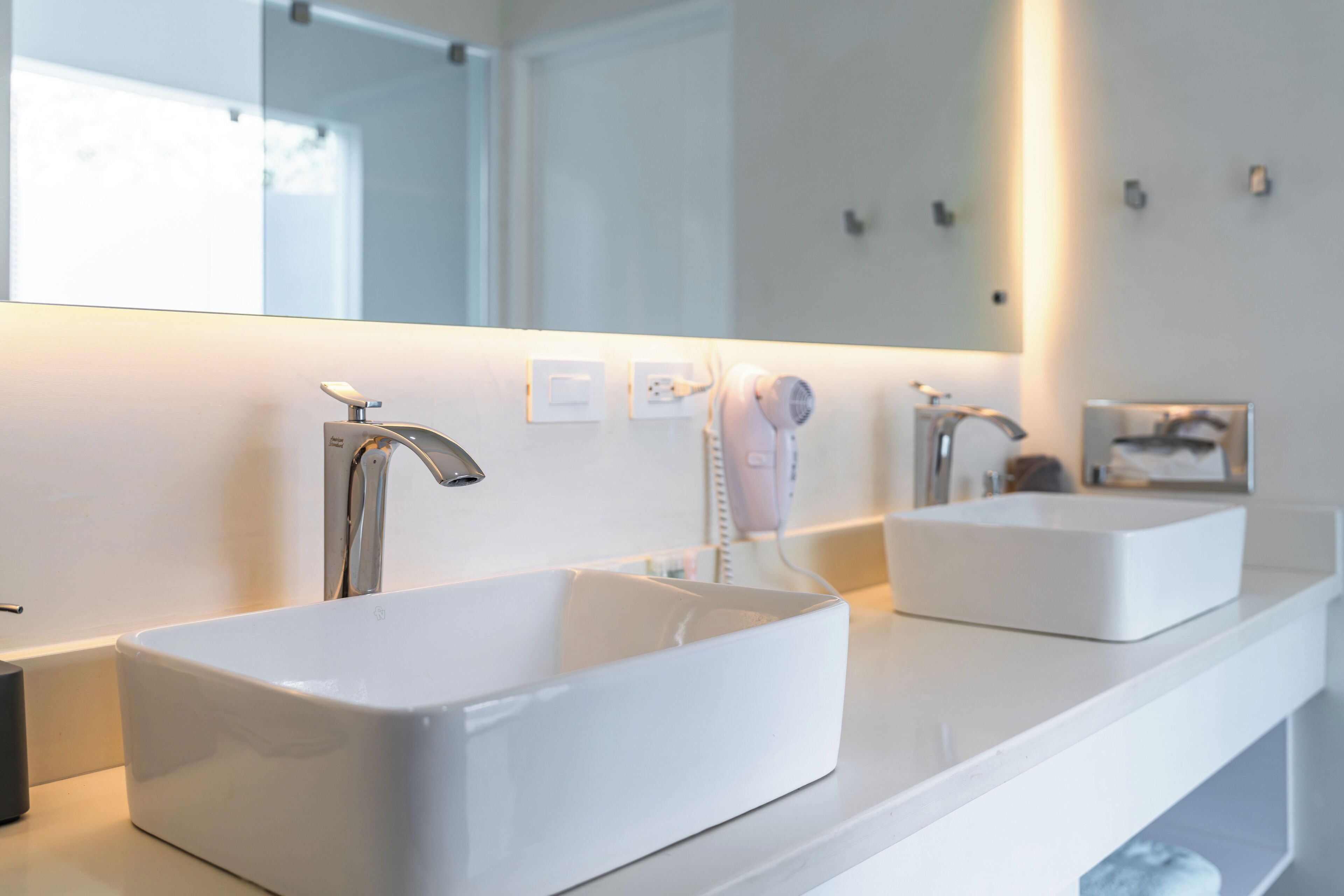 A modern bathroom with two white sinks, a large mirror, and a hairdryer on the counter.