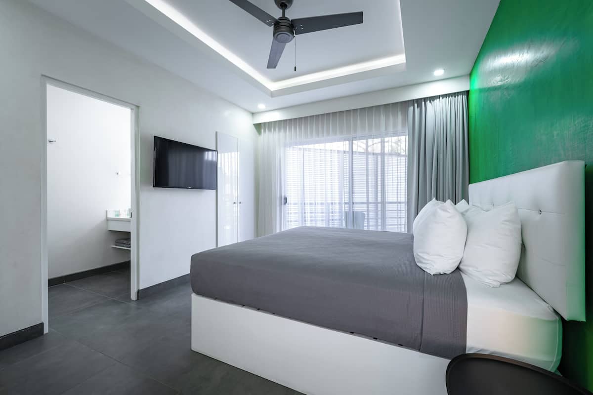 A modern bedroom with a large bed, a ceiling fan, a TV mounted on the wall, and a green accent wall.