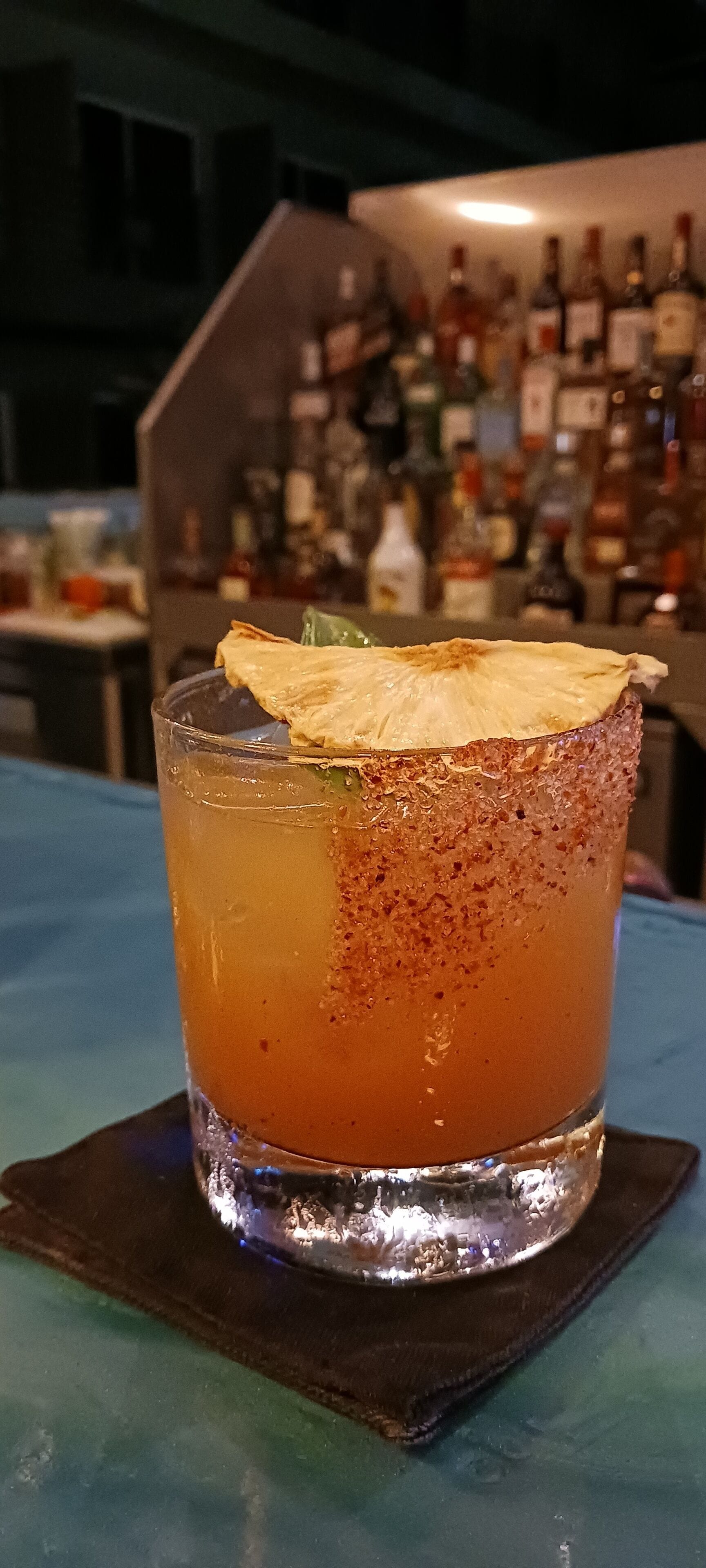 A cocktail with a salted rim, garnished with a slice of lime, on a coaster.