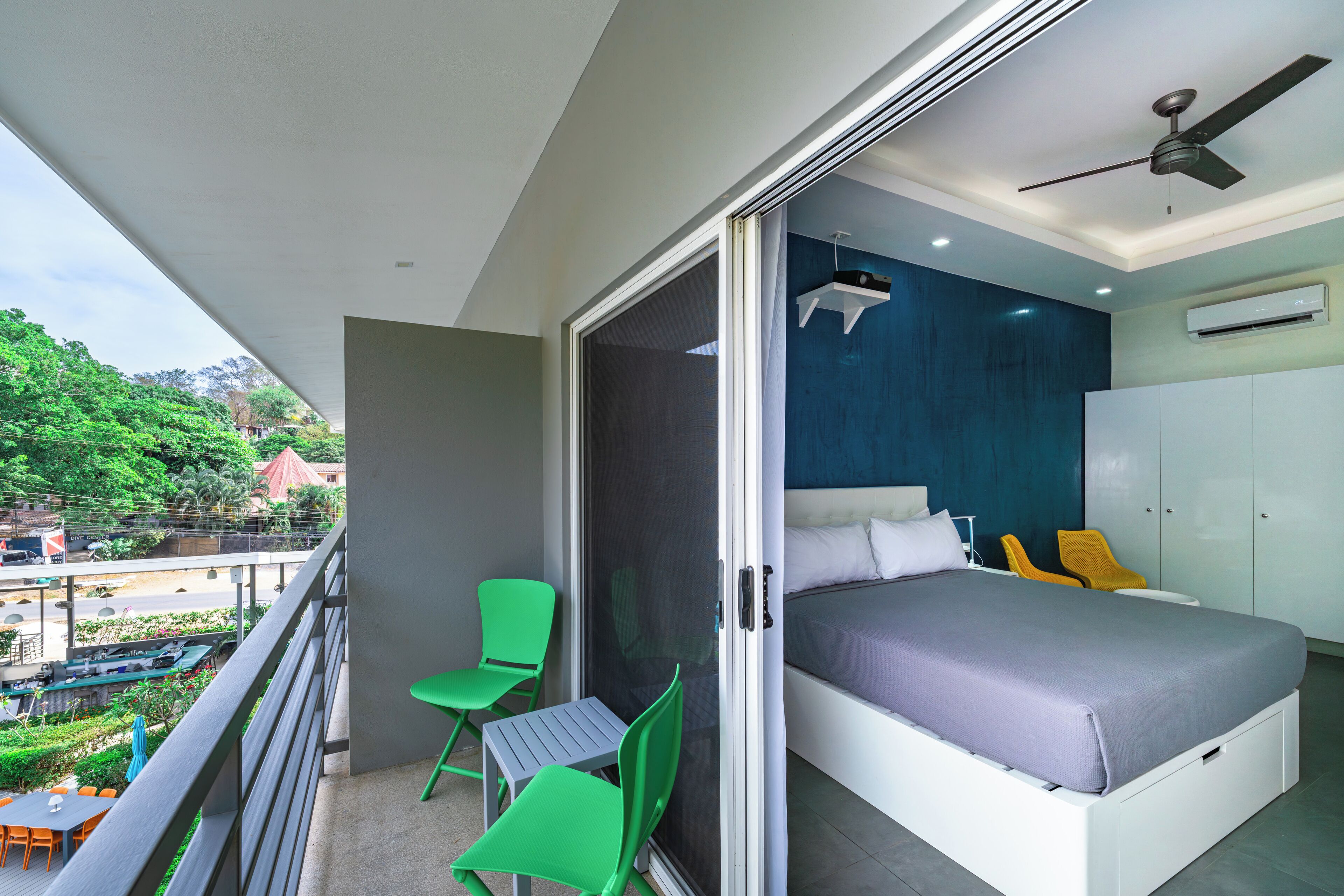 Un dormitorio con balcón, cama, ventilador de techo y aire acondicionado.