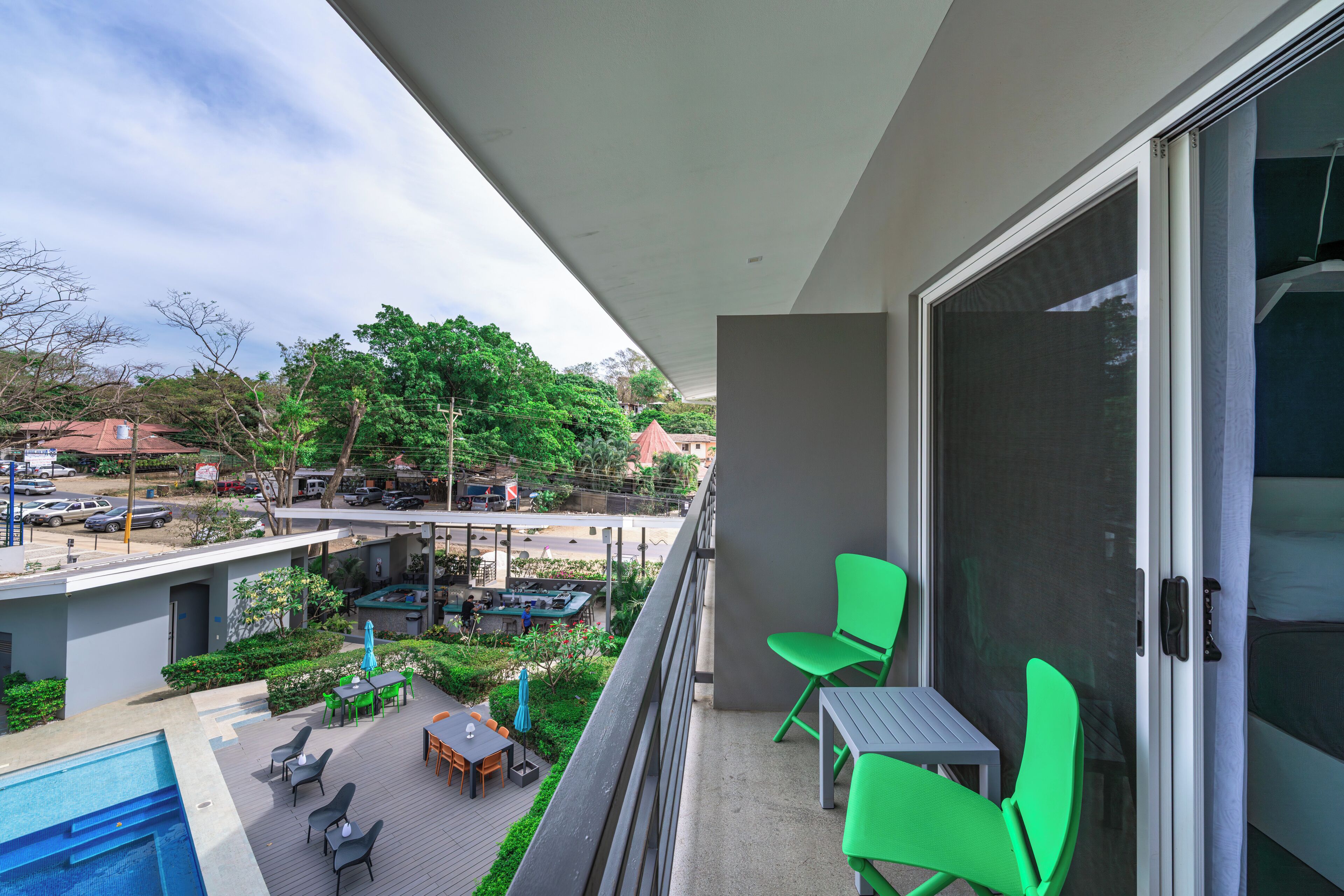 Un balcón con vistas a una piscina y zona de estar al aire libre, una puerta corrediza de vidrio y una silla verde.